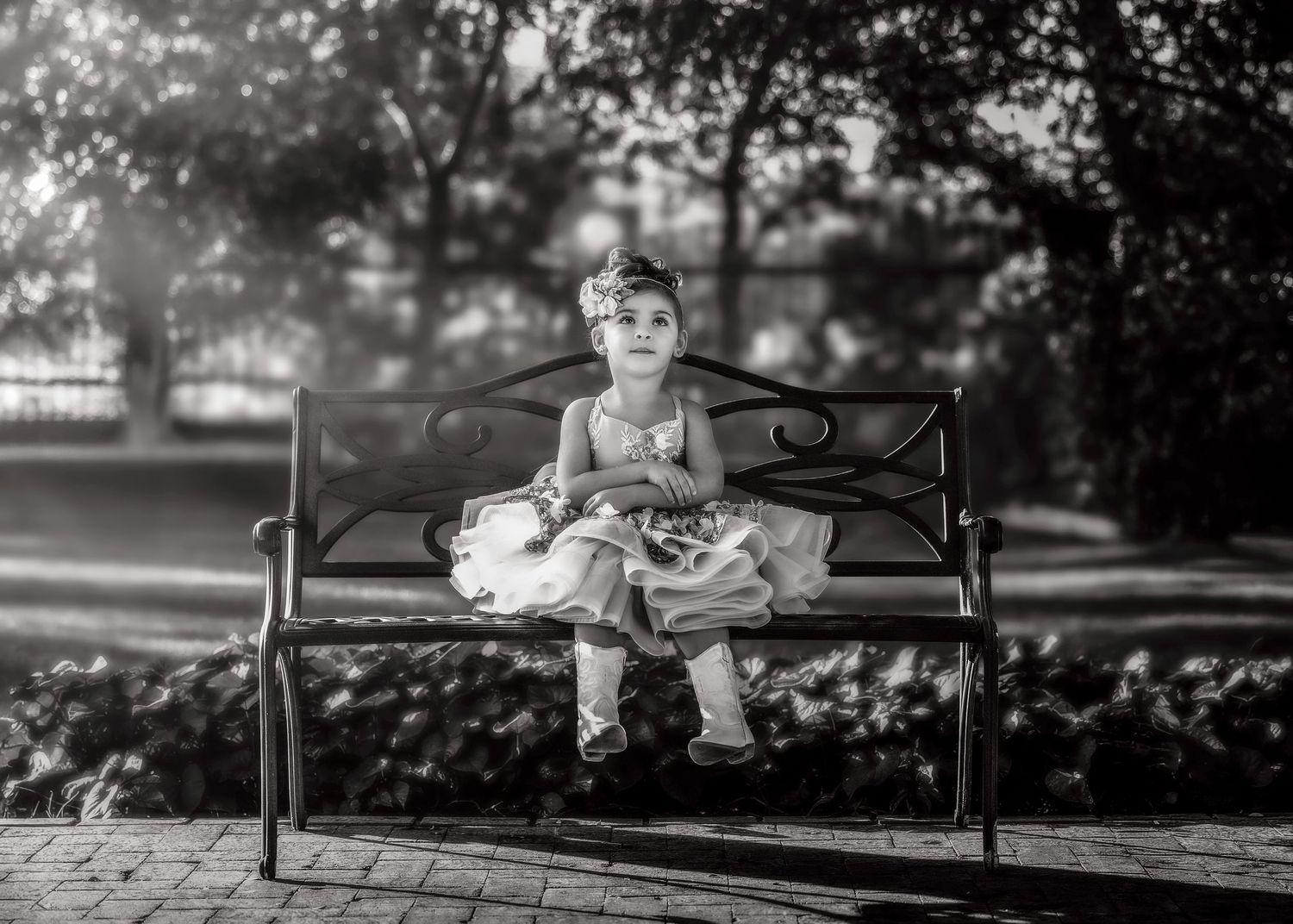 A young girl in a tutu dress sits alone on a park bench in a black and white portrait.