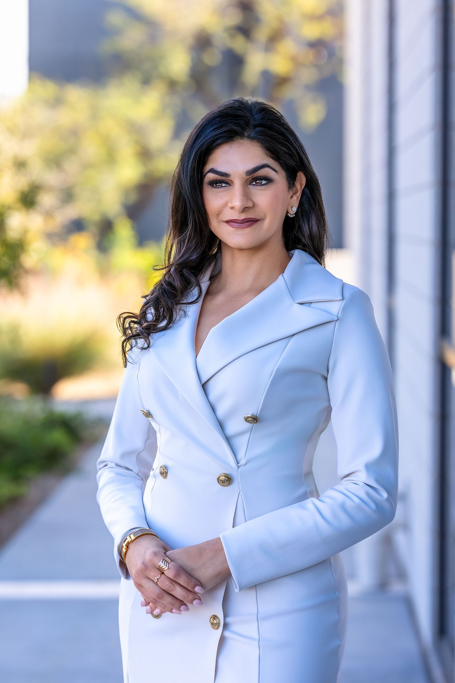 Powerful CEO and female entrepreneur standing in front of mirrored windows wearing a white coat dress. She is confident and beautiful.