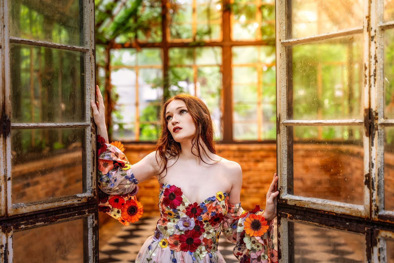 Woman in floral dress posing dramatically in vintage greenhouse doorway with red hair and bold makeup.