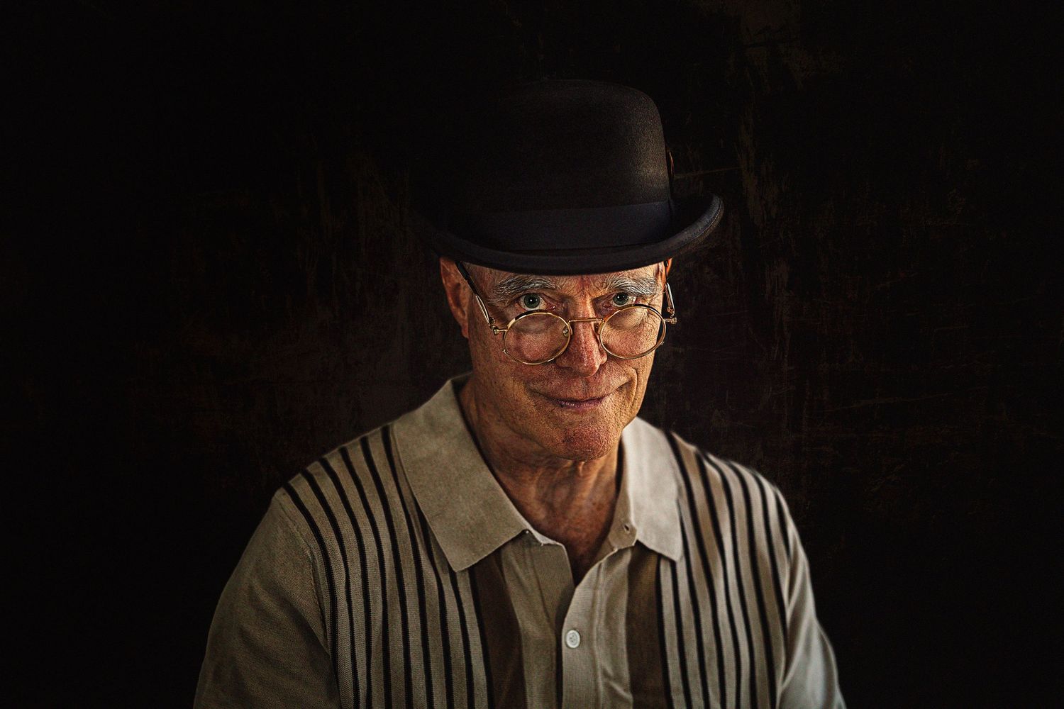 Portrait of elderly man in black bowler hat and glasses with dramatic lighting.