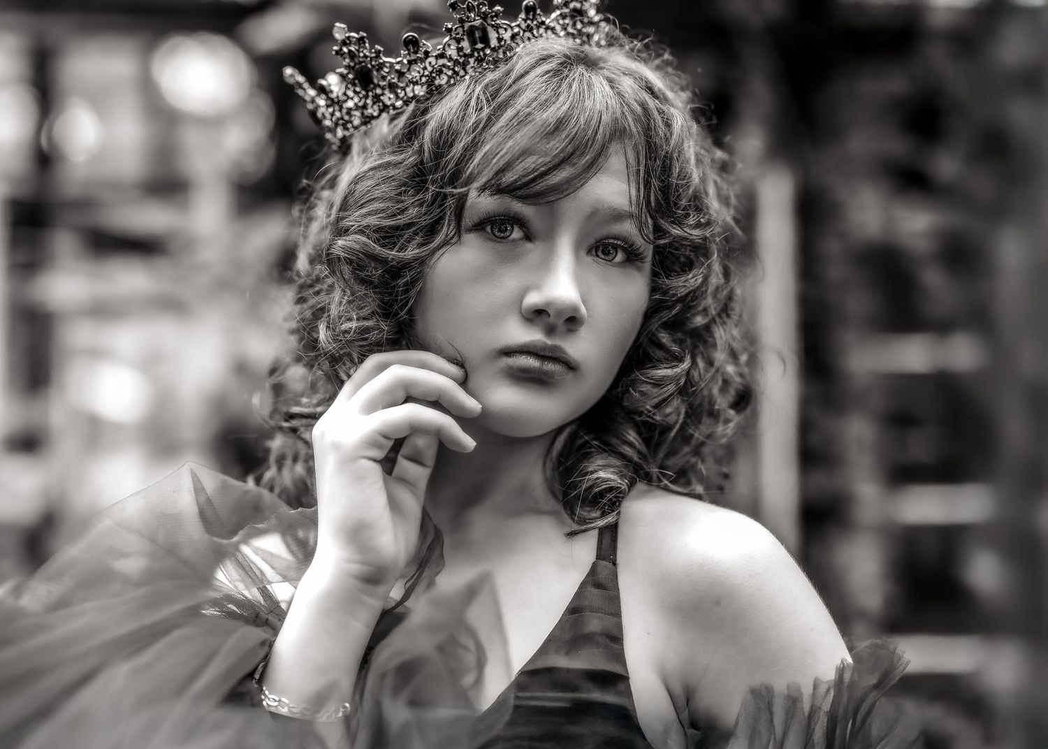 Black and white portrait of a young woman wearing a crown and elegant dress, posing gracefully with hand near face.