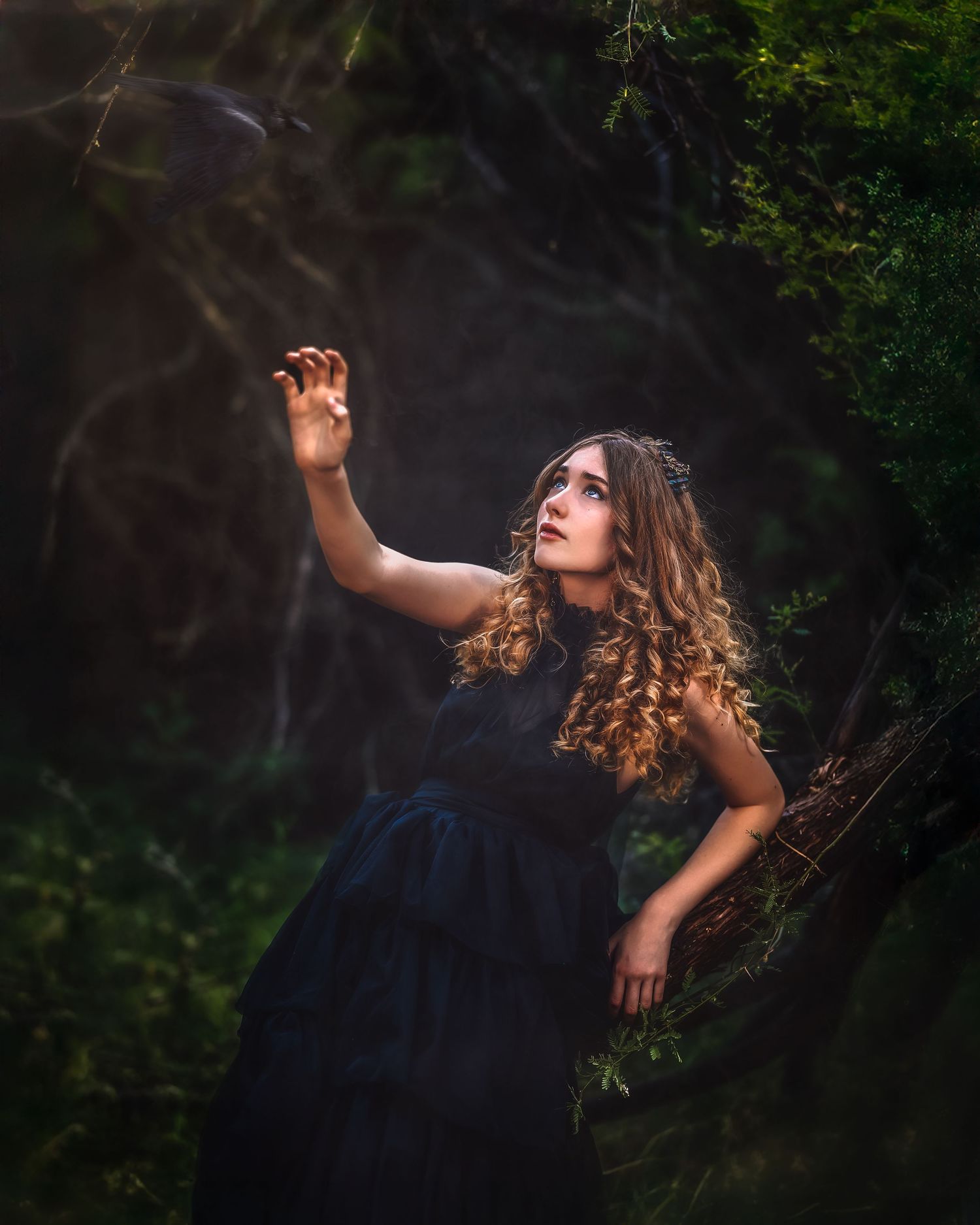 A woman in a black gown reaches upward in a mystical dark forest, with light rays filtering through lush green trees.