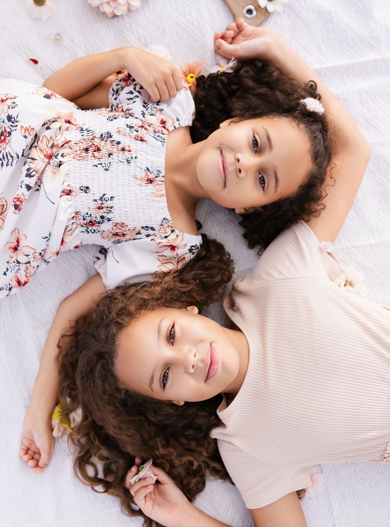 two sisters lay on a blanket and wrap their hands around the other's heads, aerial view