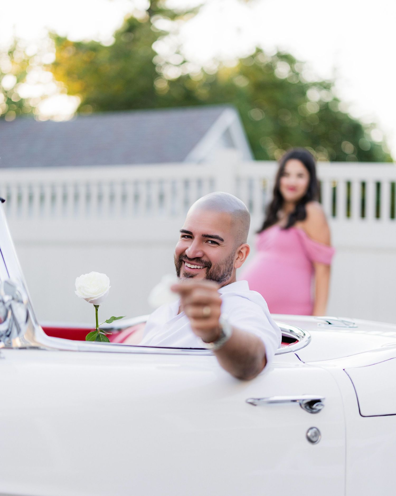 man picks petals off a white flower with wife in the background