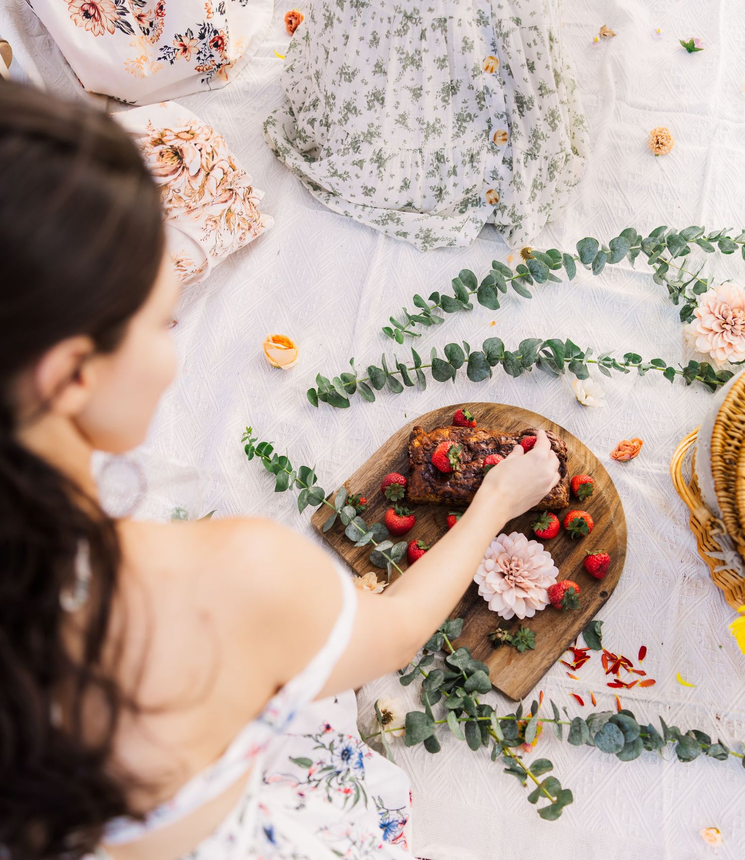 adult female placing strawberries on a wooden cutting board on a picnic blanket