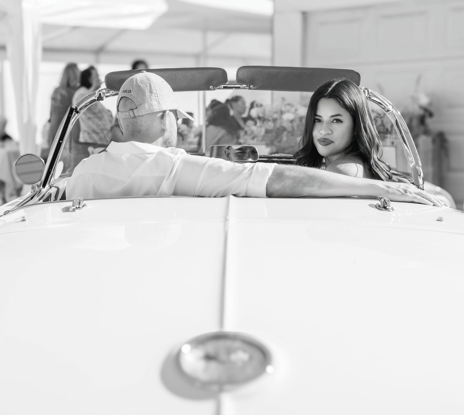 black and white photo of couple inside classic car with female looking back over her shoulder