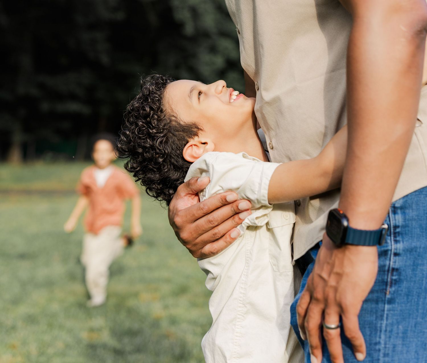 boy holds on to father with brother in the distance