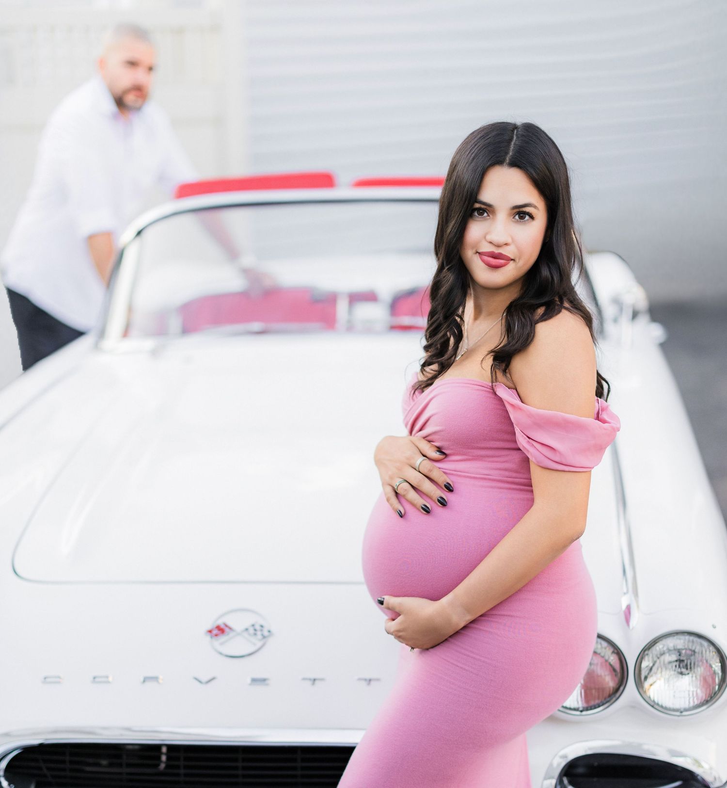 female holds pregnant belly while husband is in the background