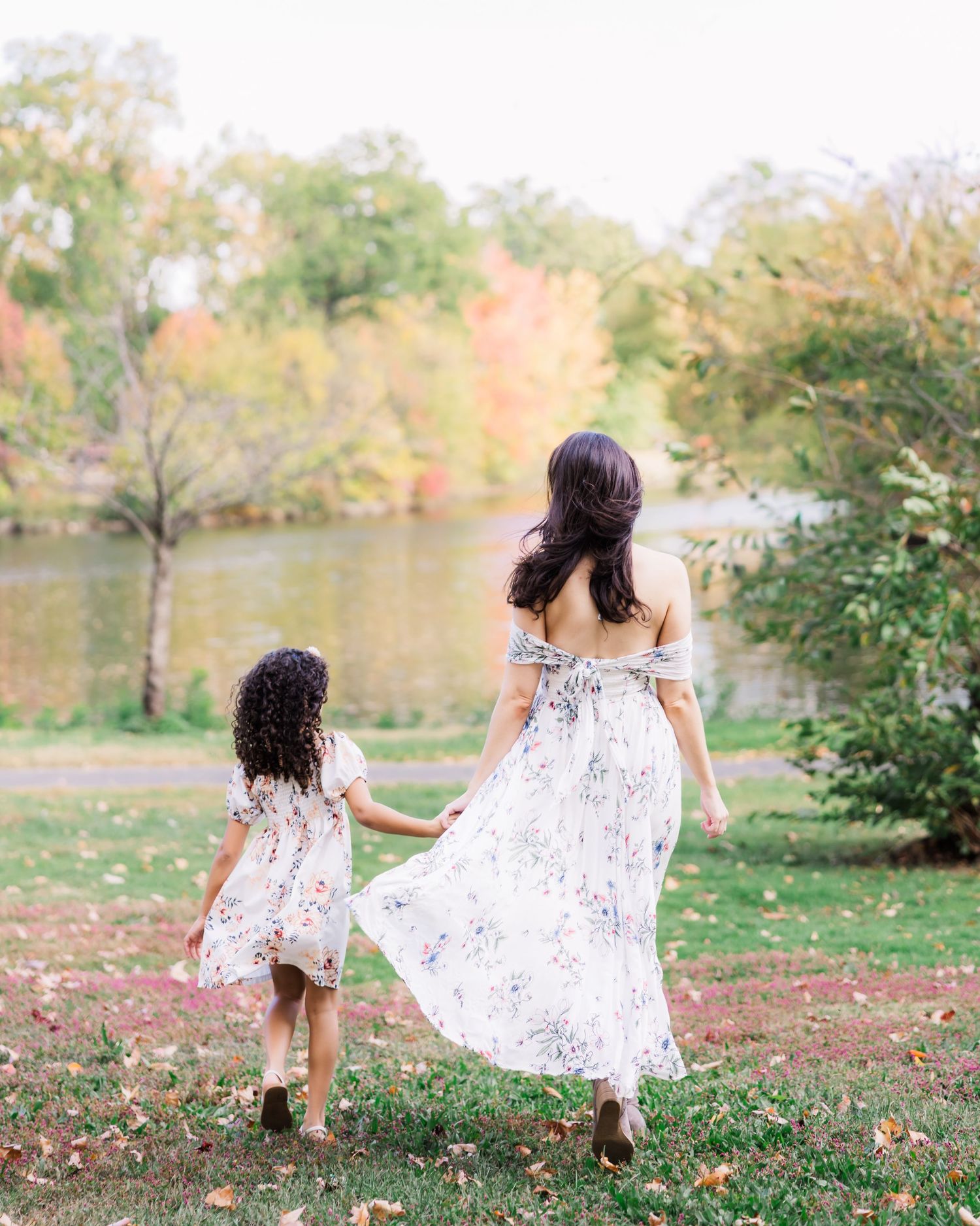 mother and daughter holds hands while walking towards a lake.