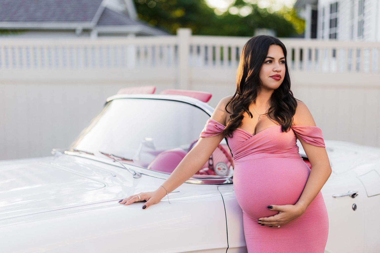 female holds belly and leans against classic car
