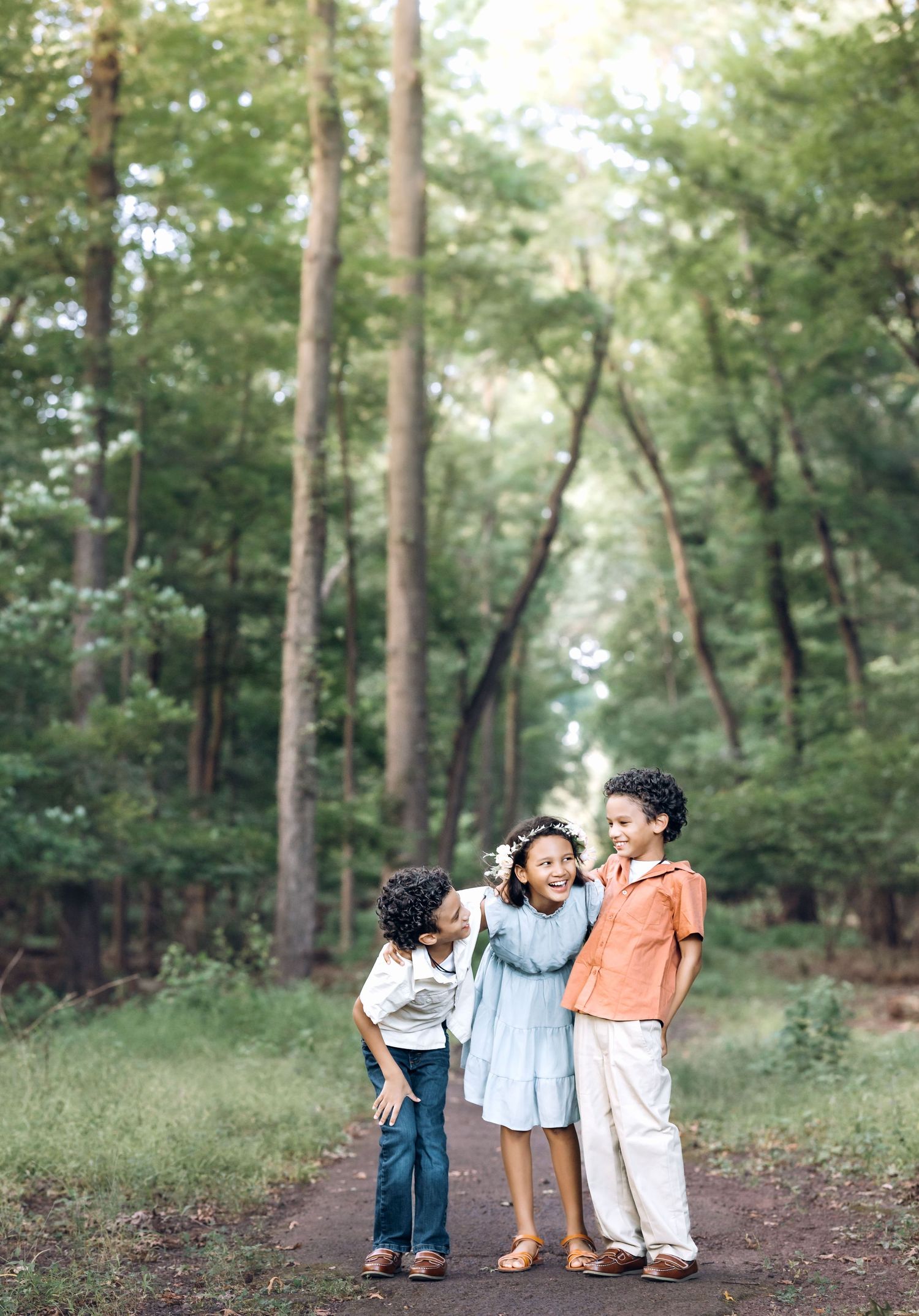 two boys and one girl, all school-aged, standing and huddled together inside a deep forest, sharing a laugh