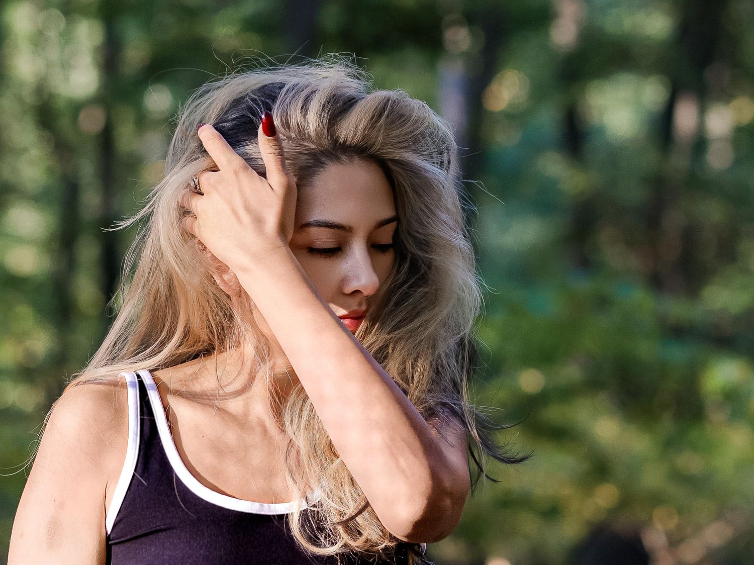 female running her left hand through her hair with her eyes closed inside a forests