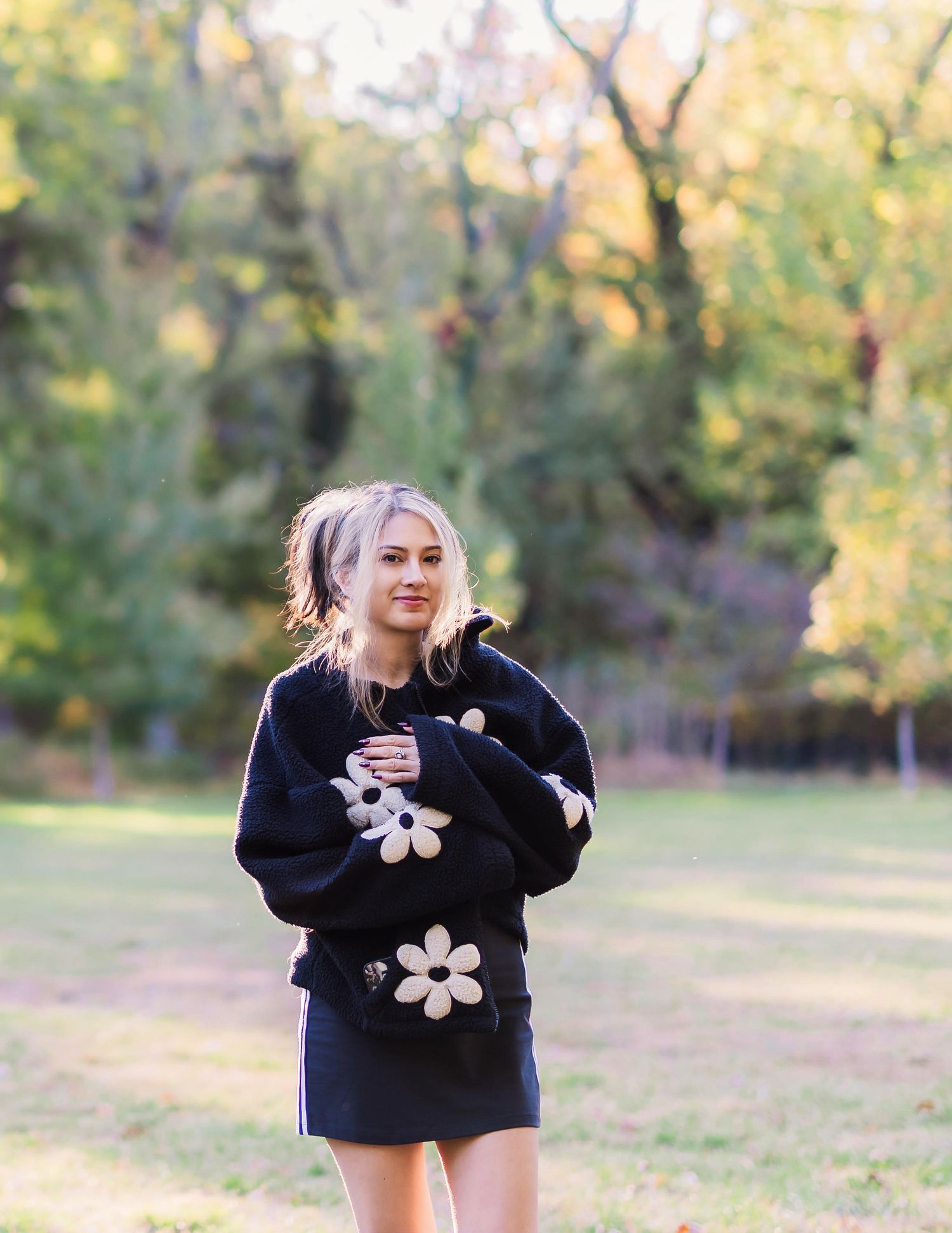 portrait of young adult female wearing oversized back fleece coat with white flower design in a fall-like setting