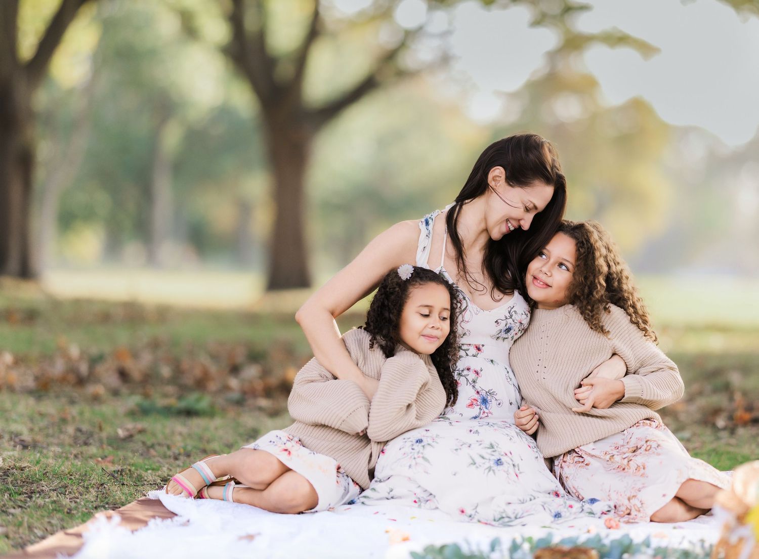mother and two daughters sit on blanket