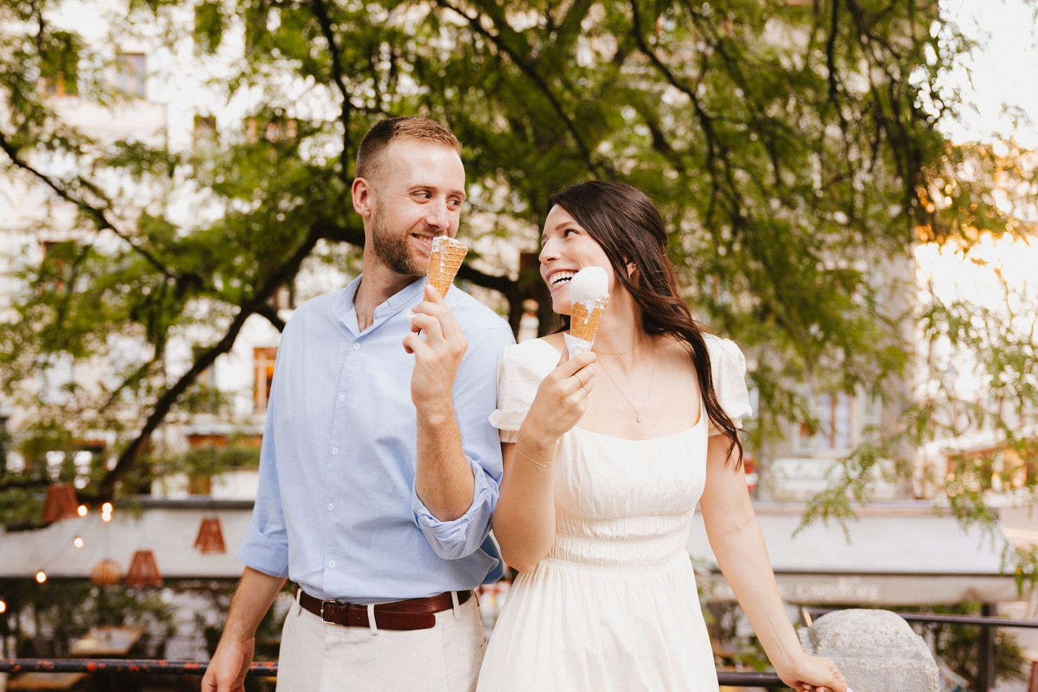 Romantic couple sharing laughs during outdoor photoshoot with trees in background.