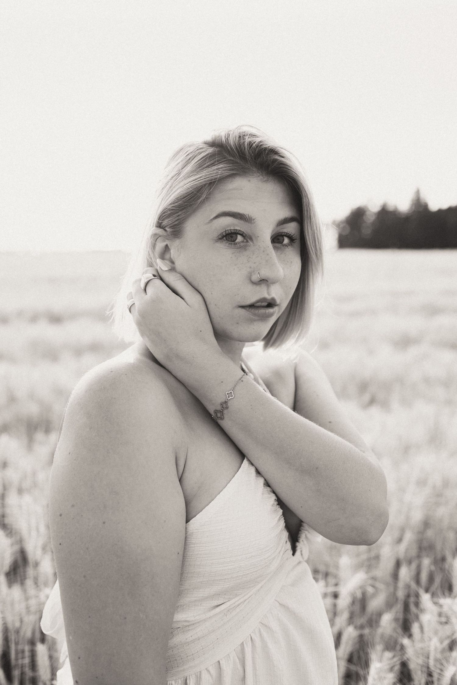 Woman in white dress poses thoughtfully in a wheat field at sunset.