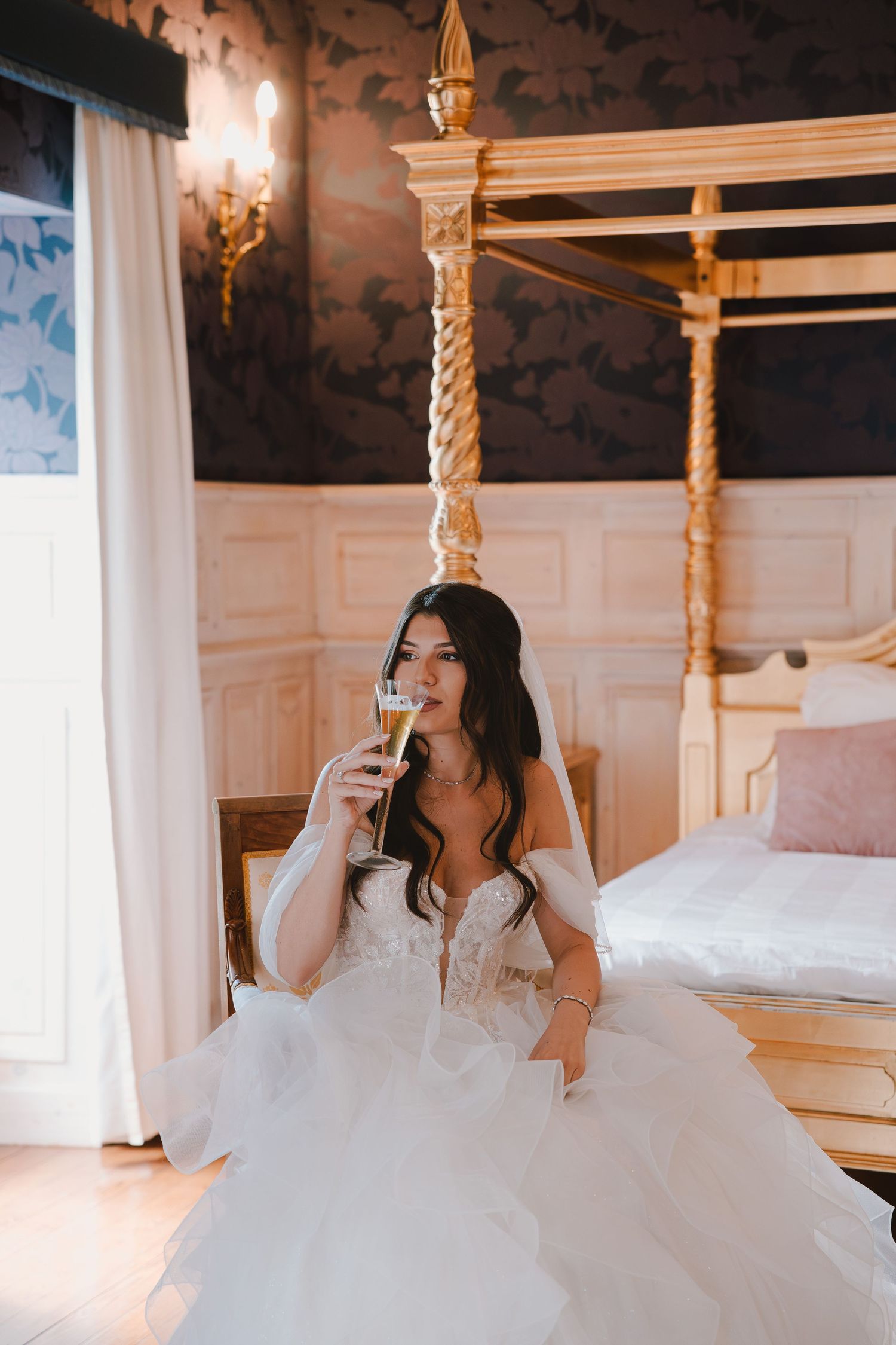 Bride in flowing white gown relaxing in an ornate room with golden pillars.