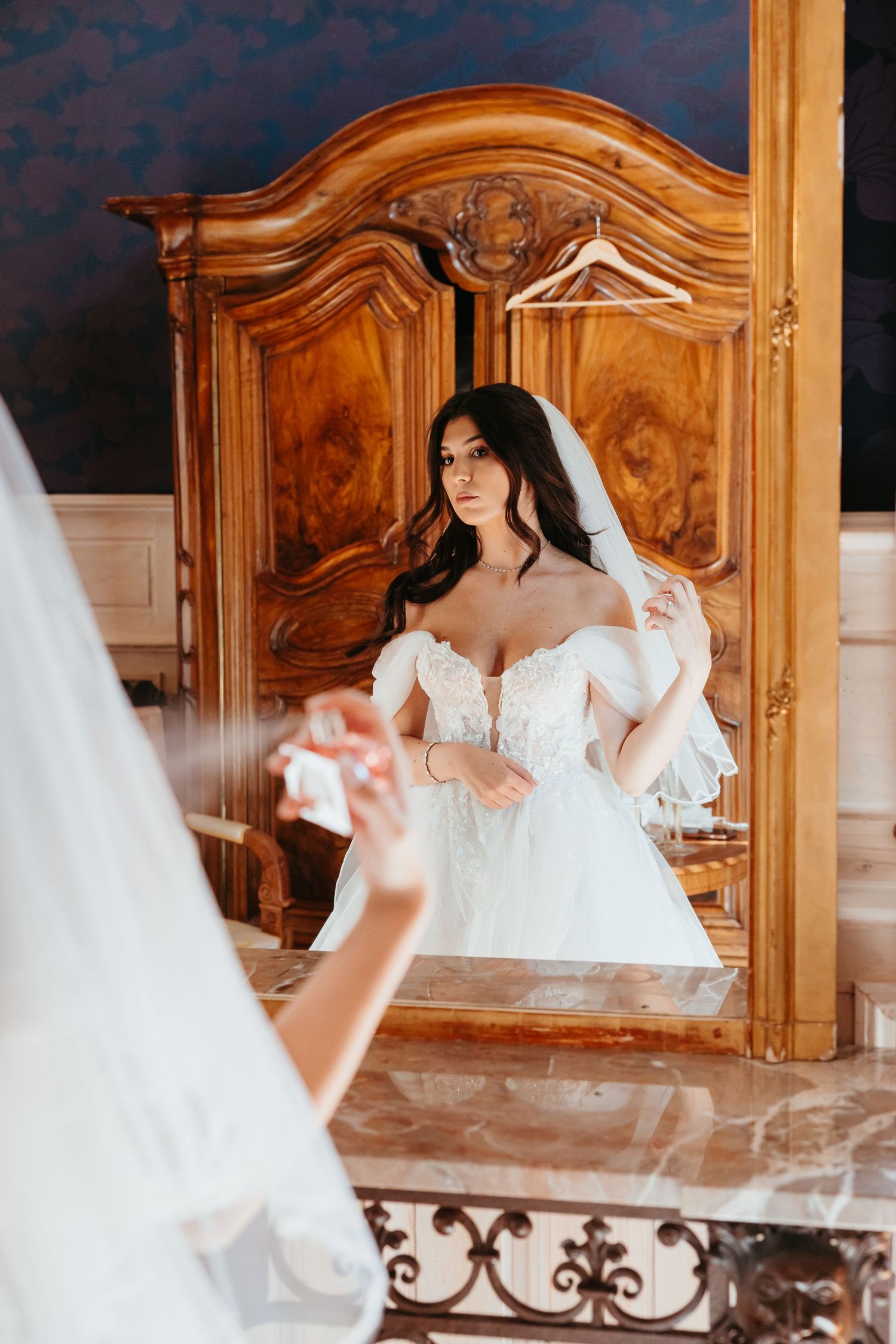 A stunning white wedding gown is reflected in an ornate vintage mirror with carved wooden frame details.