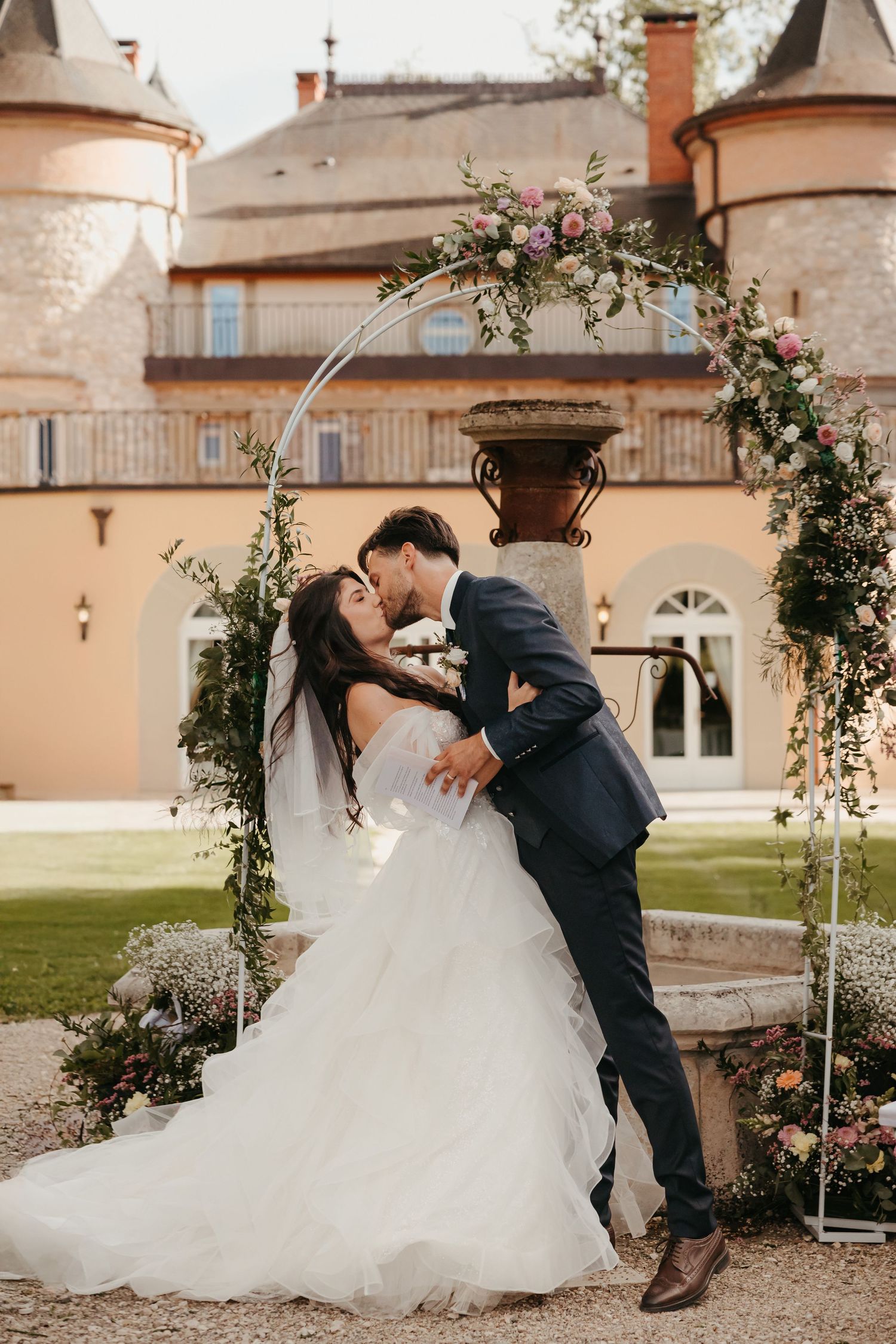 Romantic wedding portraits under a floral arch in a classic courtyard setting.