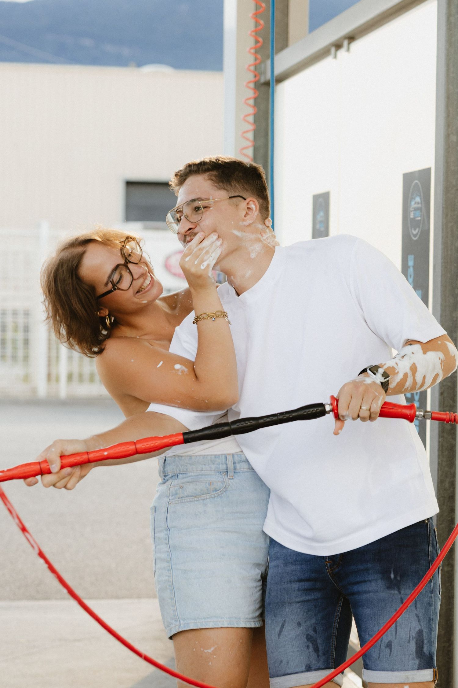 Playful couple posing with red handrails against white building exterior.