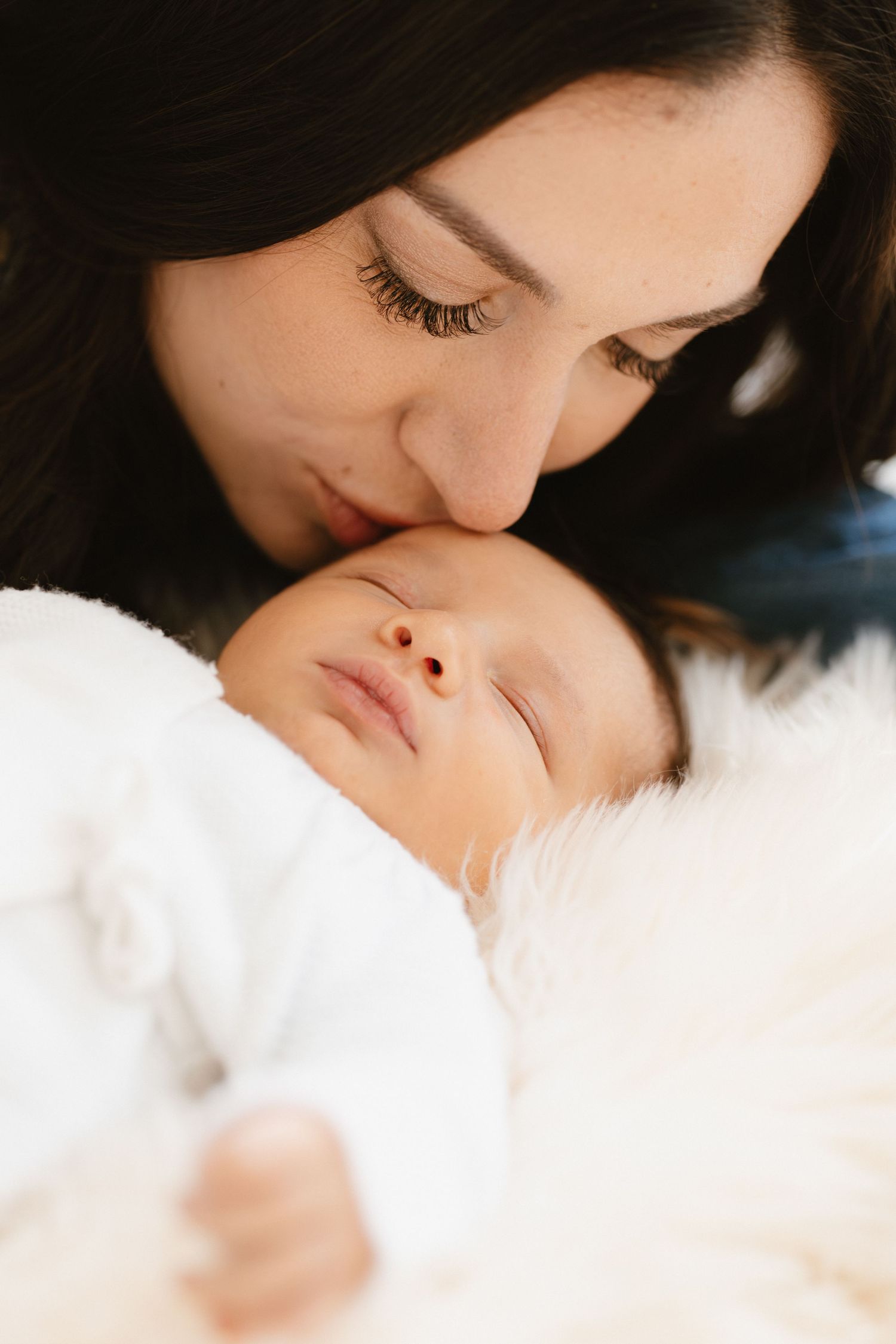 A tender moment captured in soft lighting as a parent gently kisses a sleeping baby on white bedding.