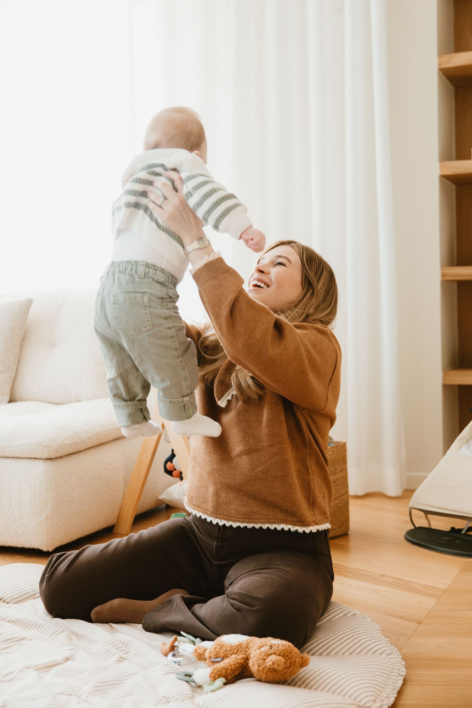 Parent and baby playing together on a cozy rug with a cat nearby in a bright living room.