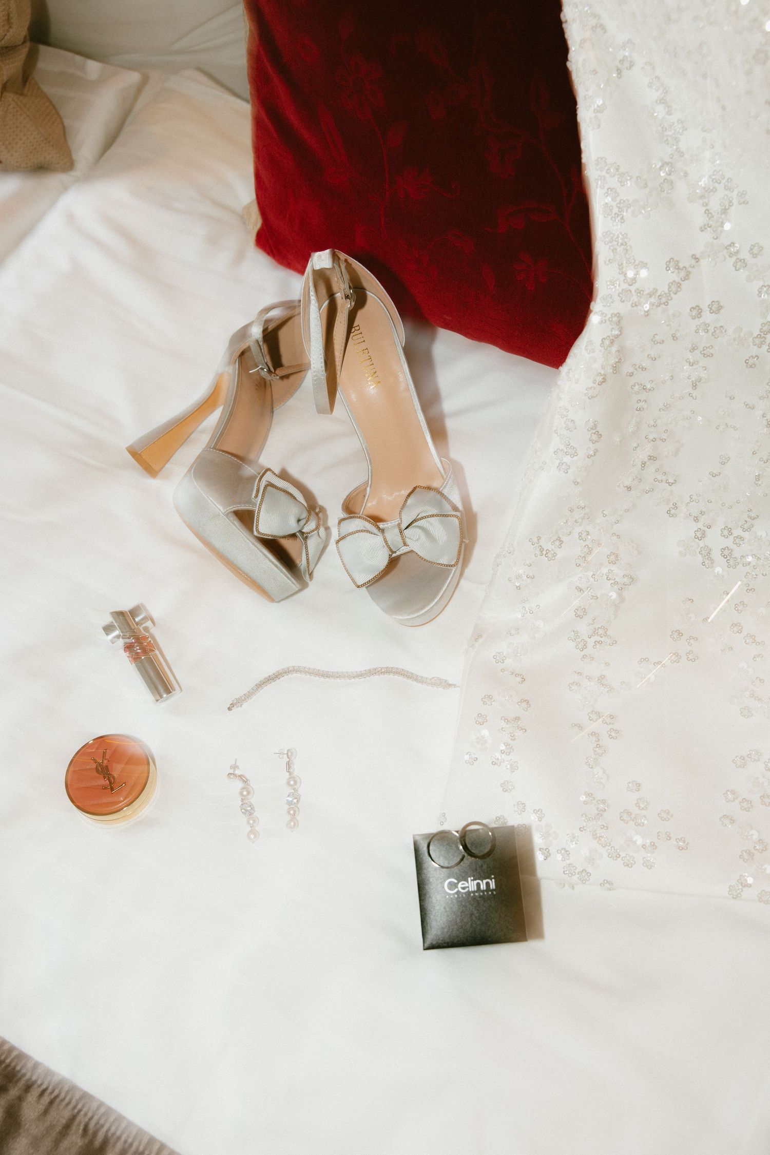 Elegant silver strappy heels and a red velvet accessory arranged on white lace fabric with a small camera.