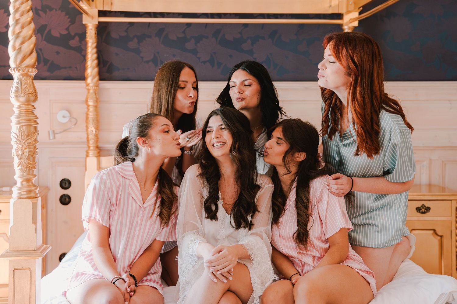 Group of bridesmaids sharing laughs and drinks in an elegantly decorated room.