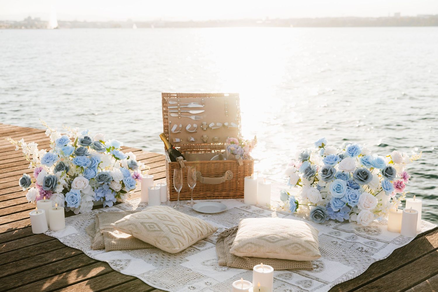Elegant wedding reception table by the ocean with blue and white floral centerpieces and candles at sunset.