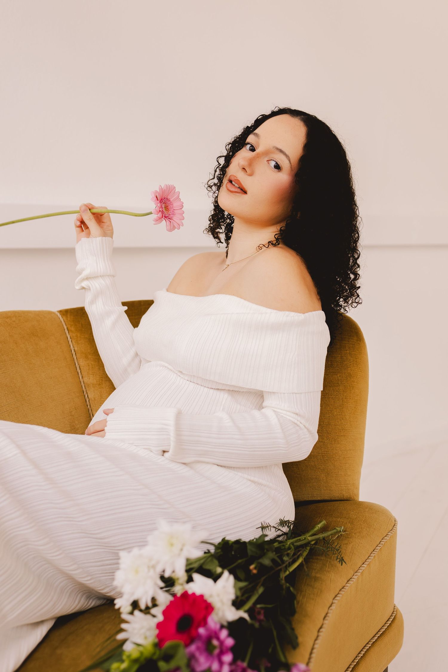 Elegant maternity photos on brown chair with pink and white flowers.