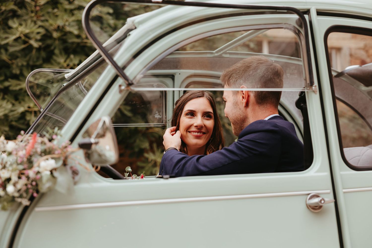 A vintage mint green car decorated with flowers captures a romantic wedding moment.