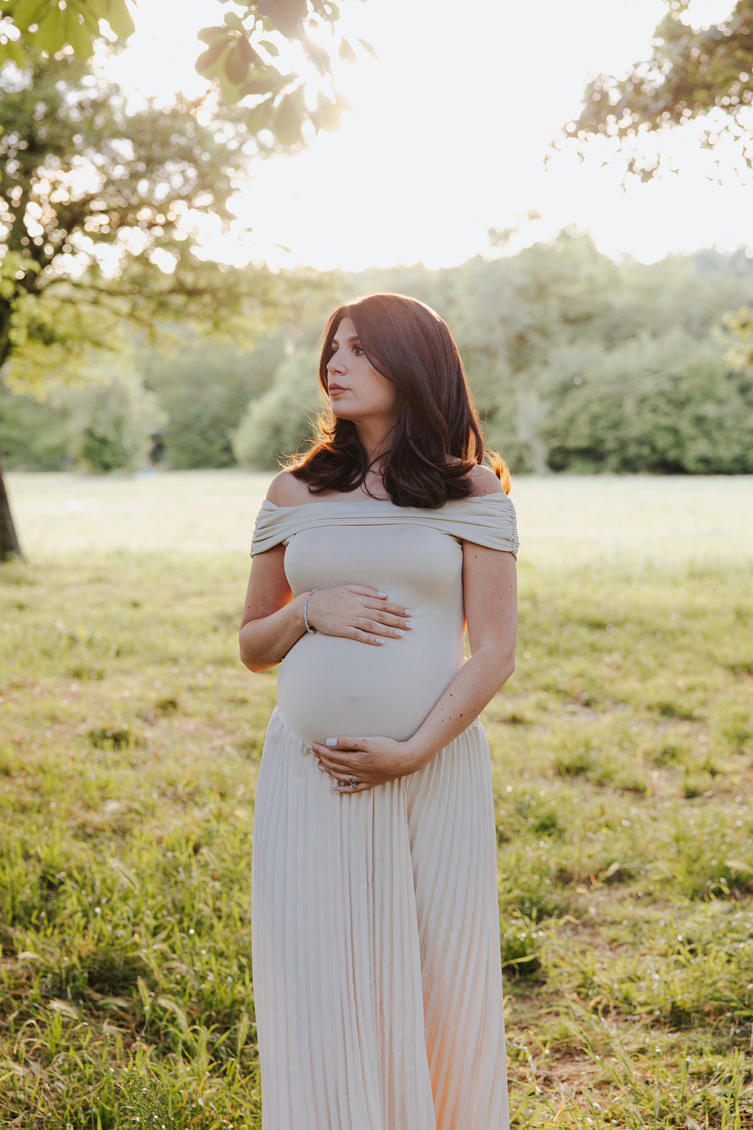 Maternity photoshoot in a sunny field with flowing white dress.