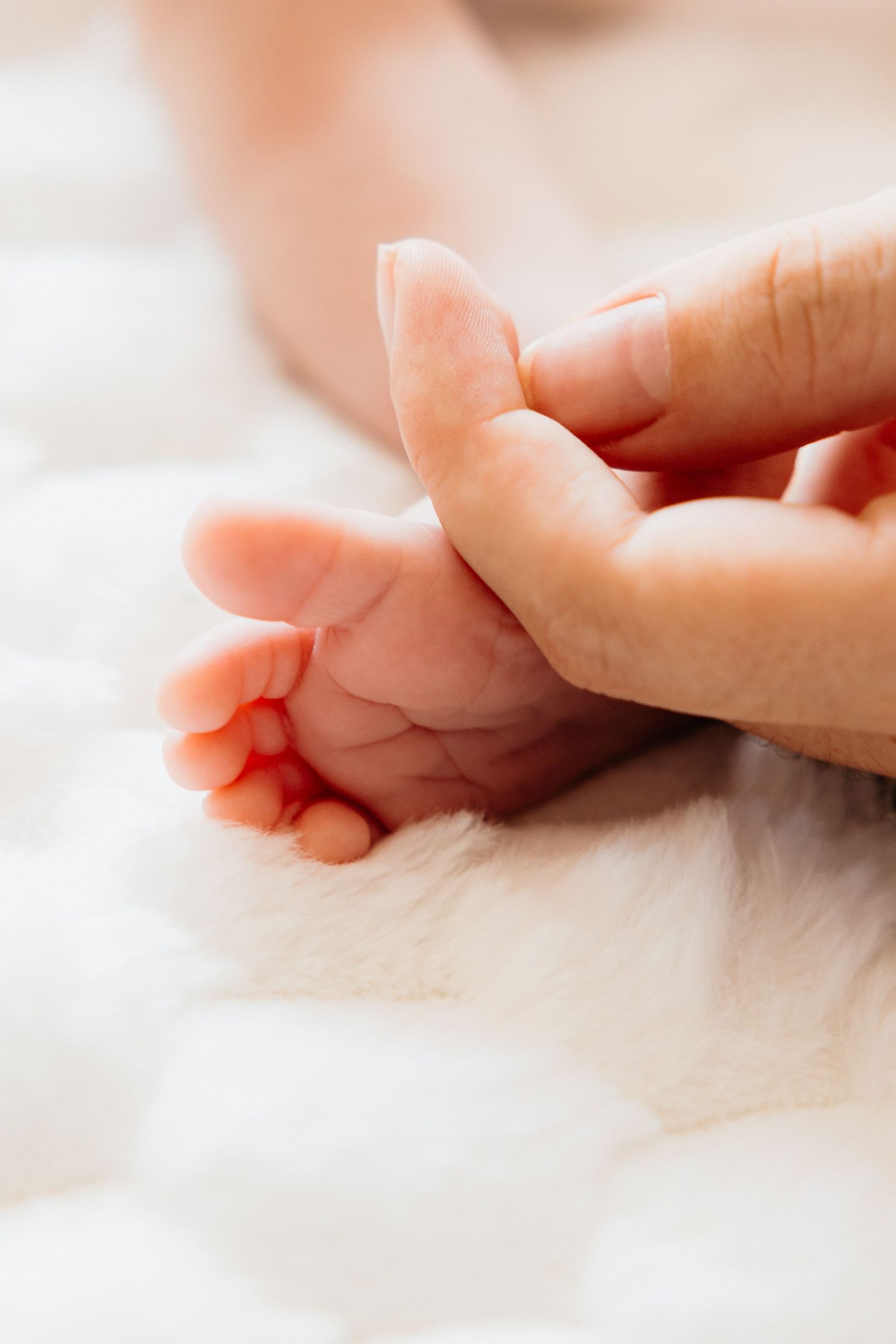 A gentle hand touches a tiny baby's foot resting on soft white fabric.