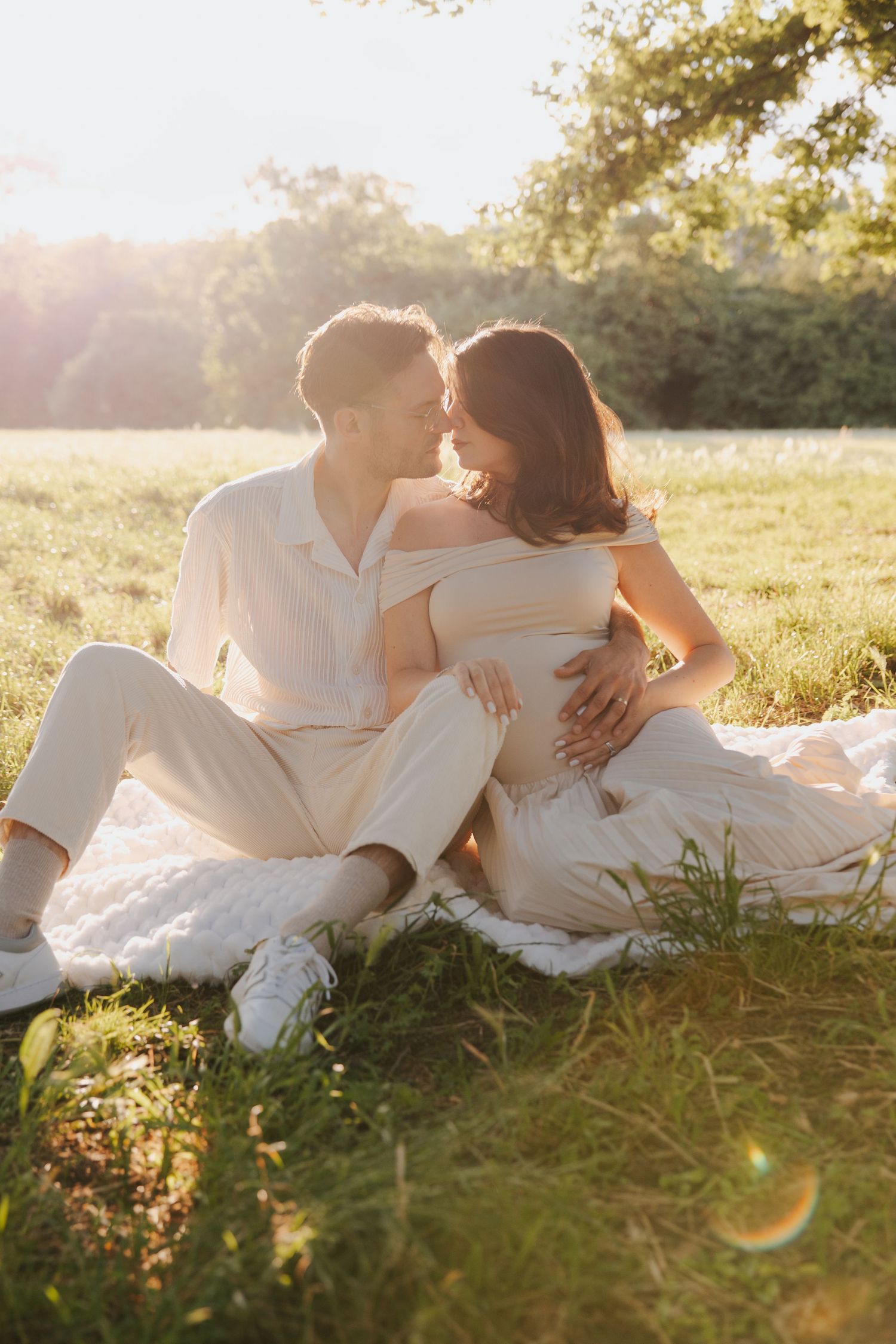Couple in white clothing lying together on grass during golden hour sunset.