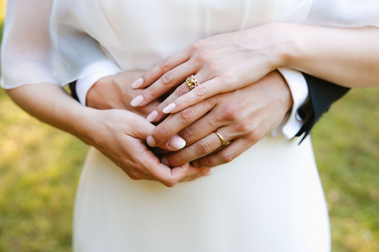 Close-up view of hands wearing wedding rings against a soft white and green background.
