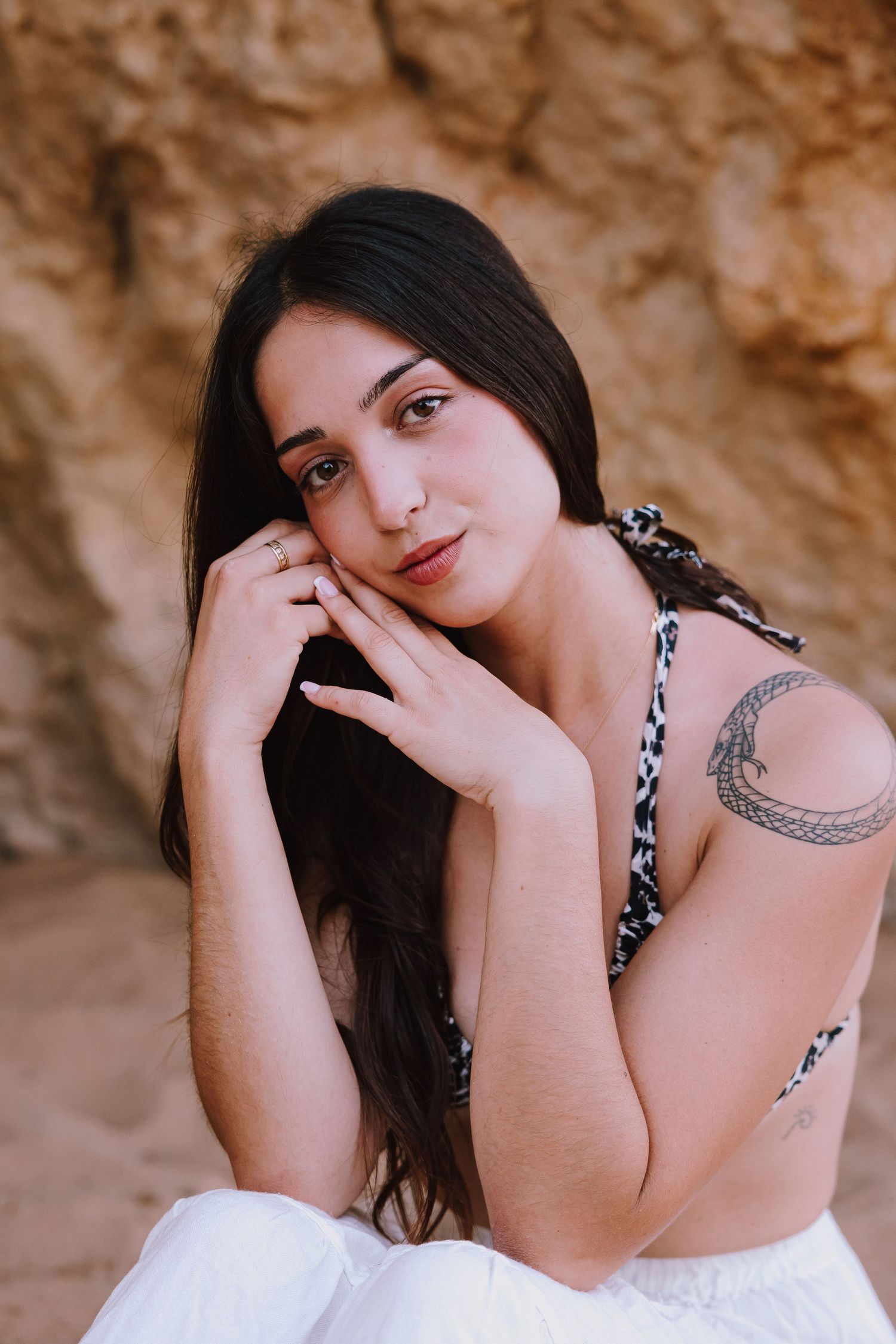 Portrait of a person with long dark hair and a tattoo against a desert rock background.