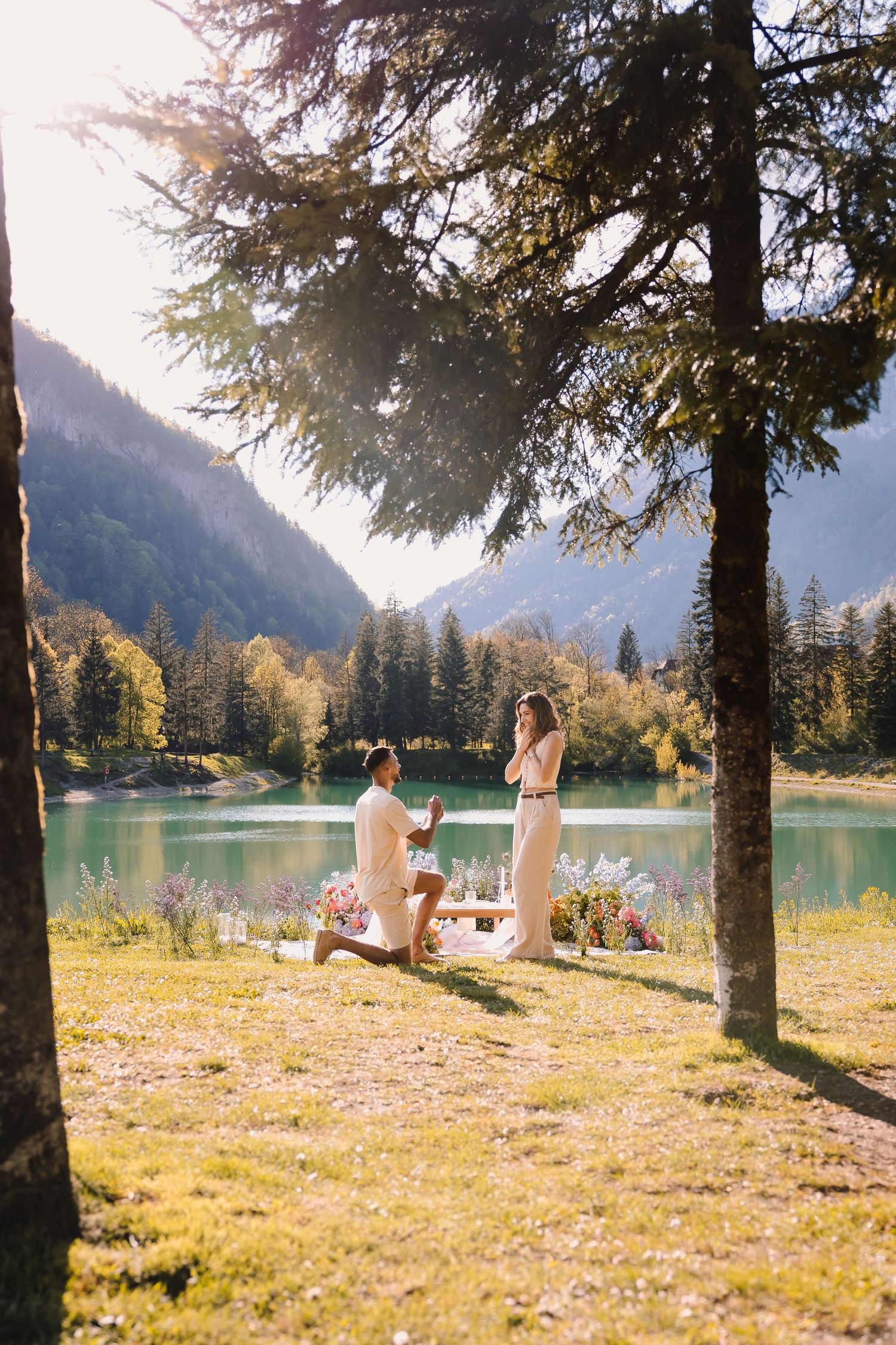 A romantic marriage proposal scene by a scenic mountain lake surrounded by evergreen trees.