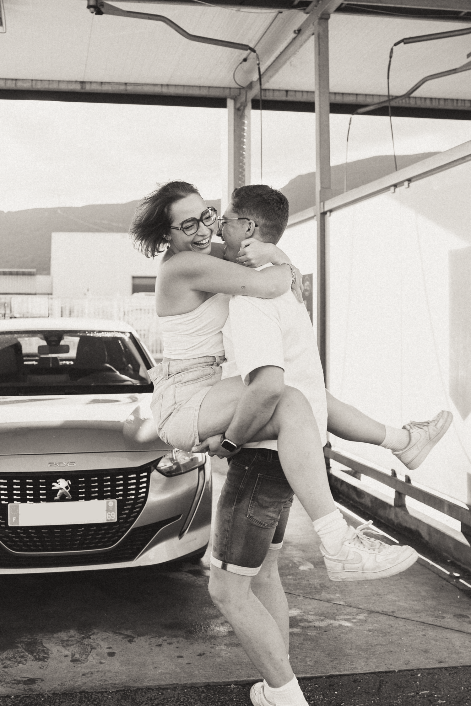 A romantic moment captured between two people in front of a parked car.
