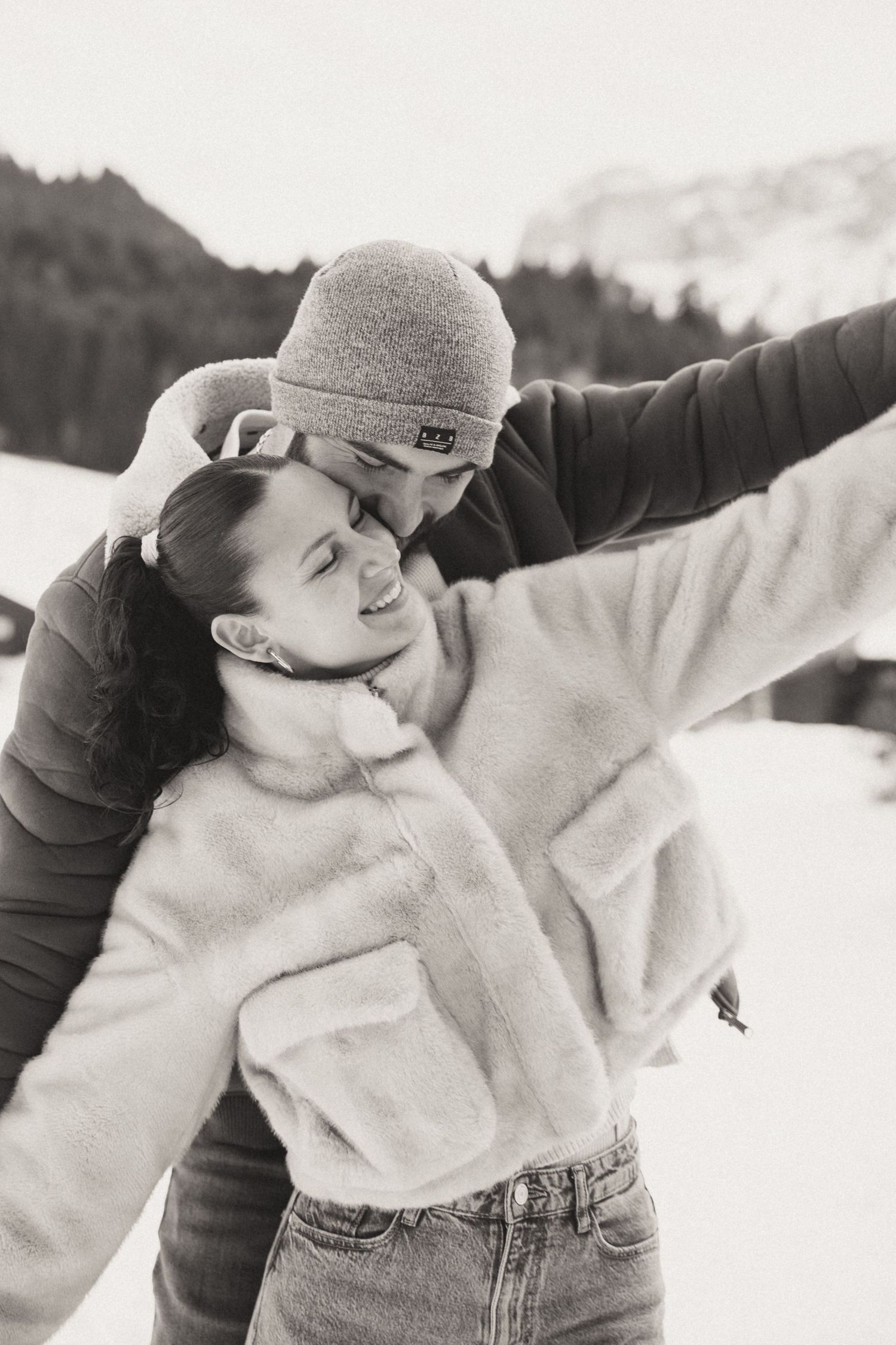 A person in a white sweater and jeans enjoys a playful winter moment in the snowy mountains.