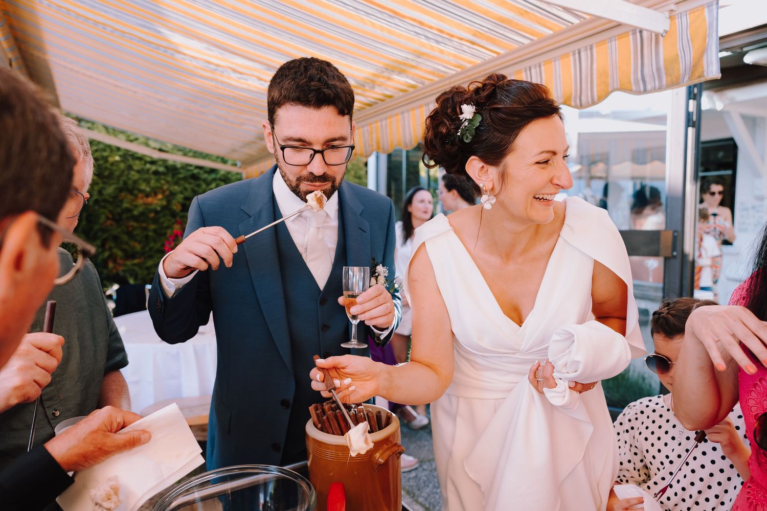 Guests enjoying drinks and conversation at an outdoor wedding reception with white table settings and natural lighting.