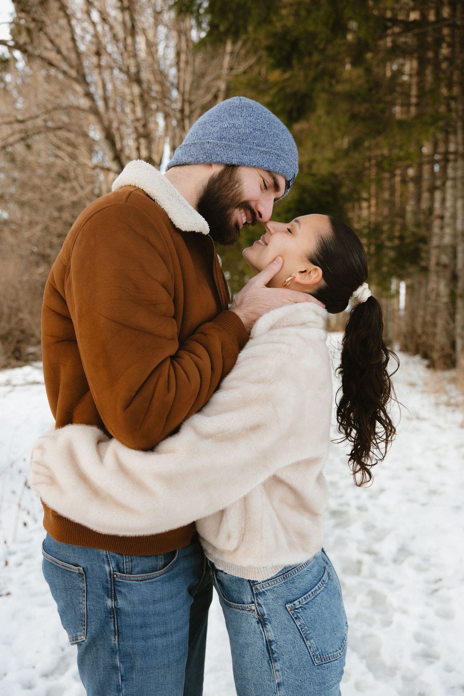 Couple in winter clothing share romantic moments in a snowy forest setting through a series of affectionate poses.