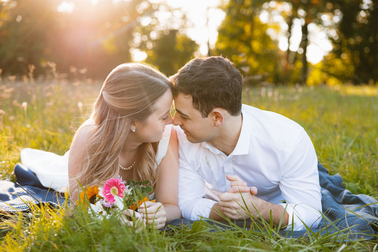 A romantic couple lies together in a sunlit meadow during golden hour, creating an intimate outdoor portrait series.
