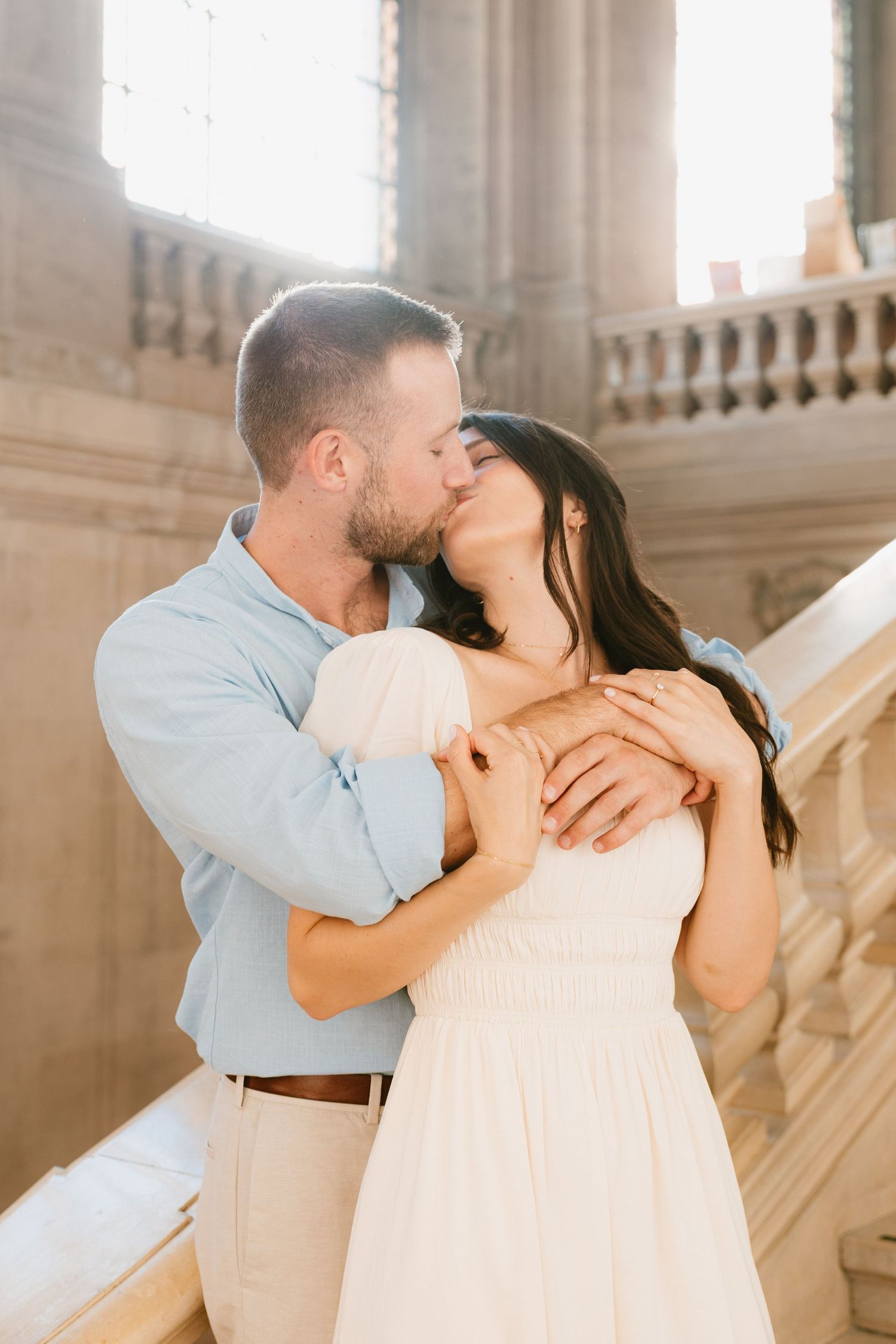 A couple shares an intimate kiss in a bright indoor setting with ornate columns and architecture.