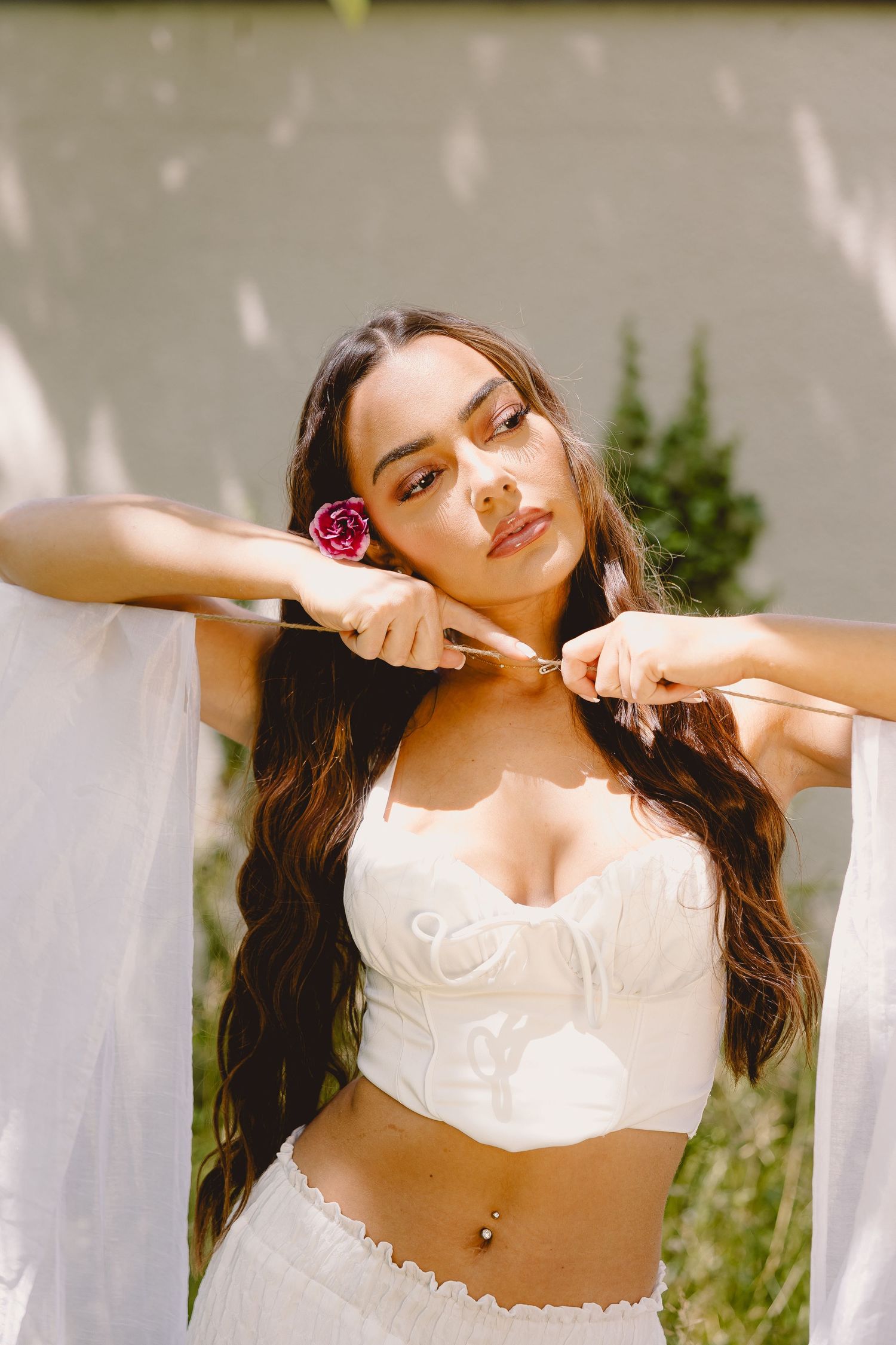 A dreamy bridal portrait in white attire with a pink rose against a soft background.