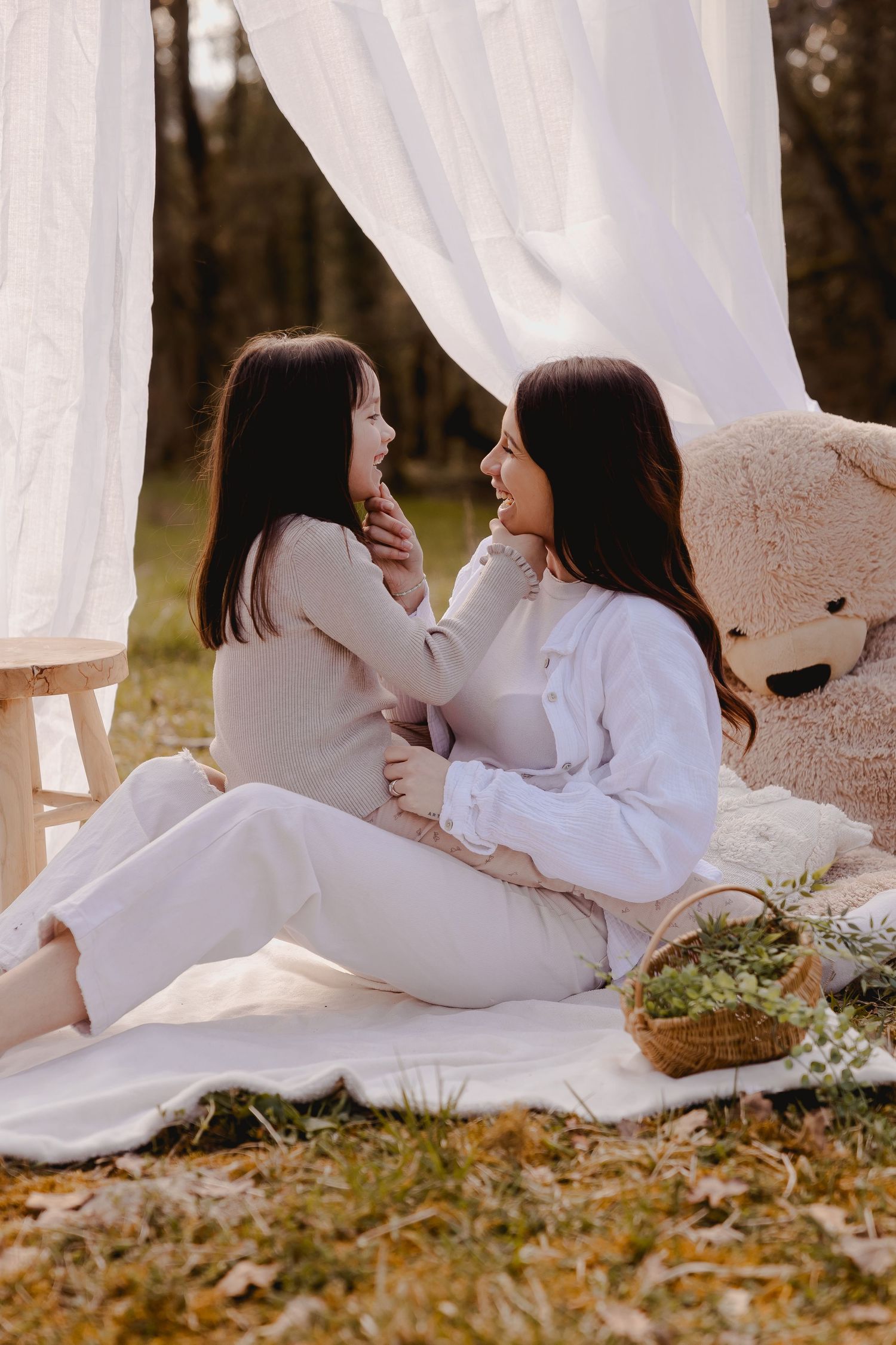 A tender moment captured on a white picnic blanket with draped fabric and floral accents.