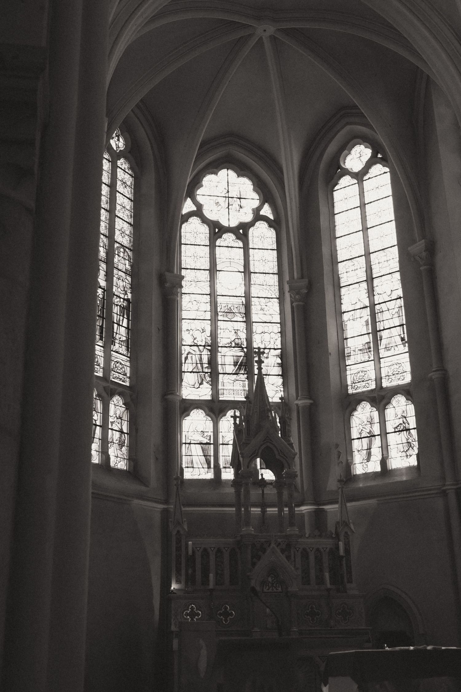 Gothic church interior with ornate stained glass windows and vaulted stone arches in dramatic black and white lighting.