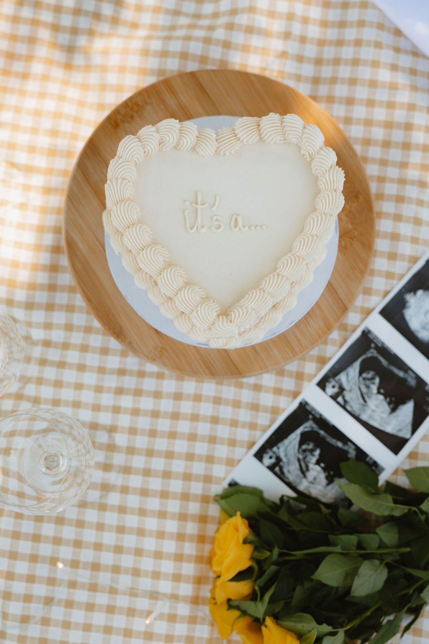 Heart-shaped ceramic plate on gingham tablecloth with yellow flowers and photographs.