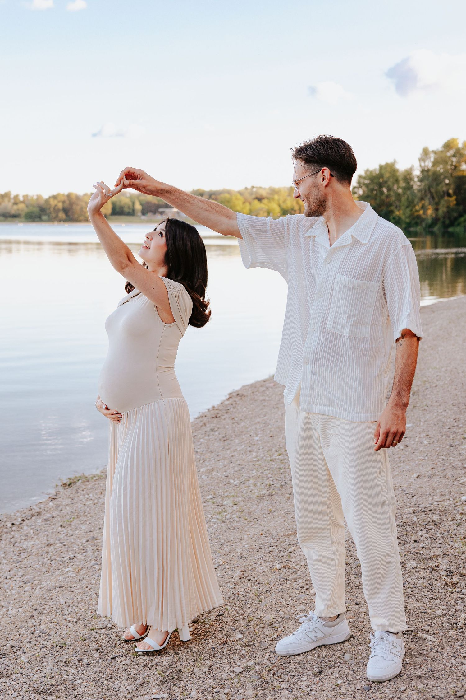 Couple in white outfits dancing joyfully on a beach at sunset.
