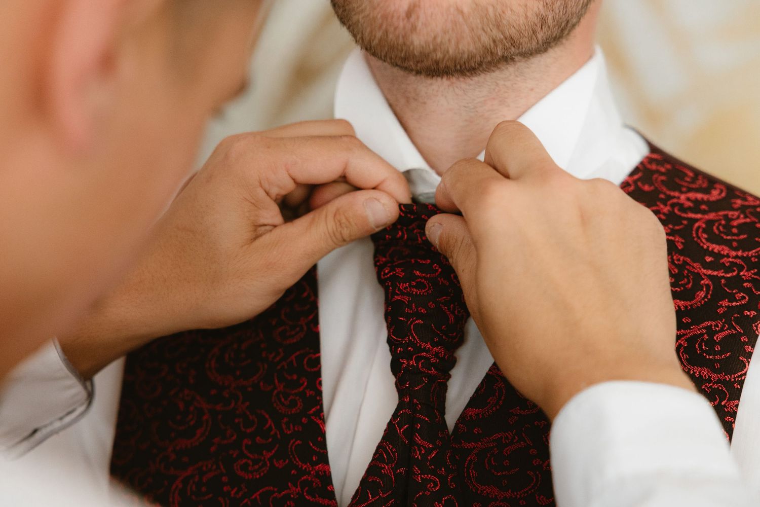 Close-up sequence showing someone adjusting a black and red patterned necktie against a white dress shirt.