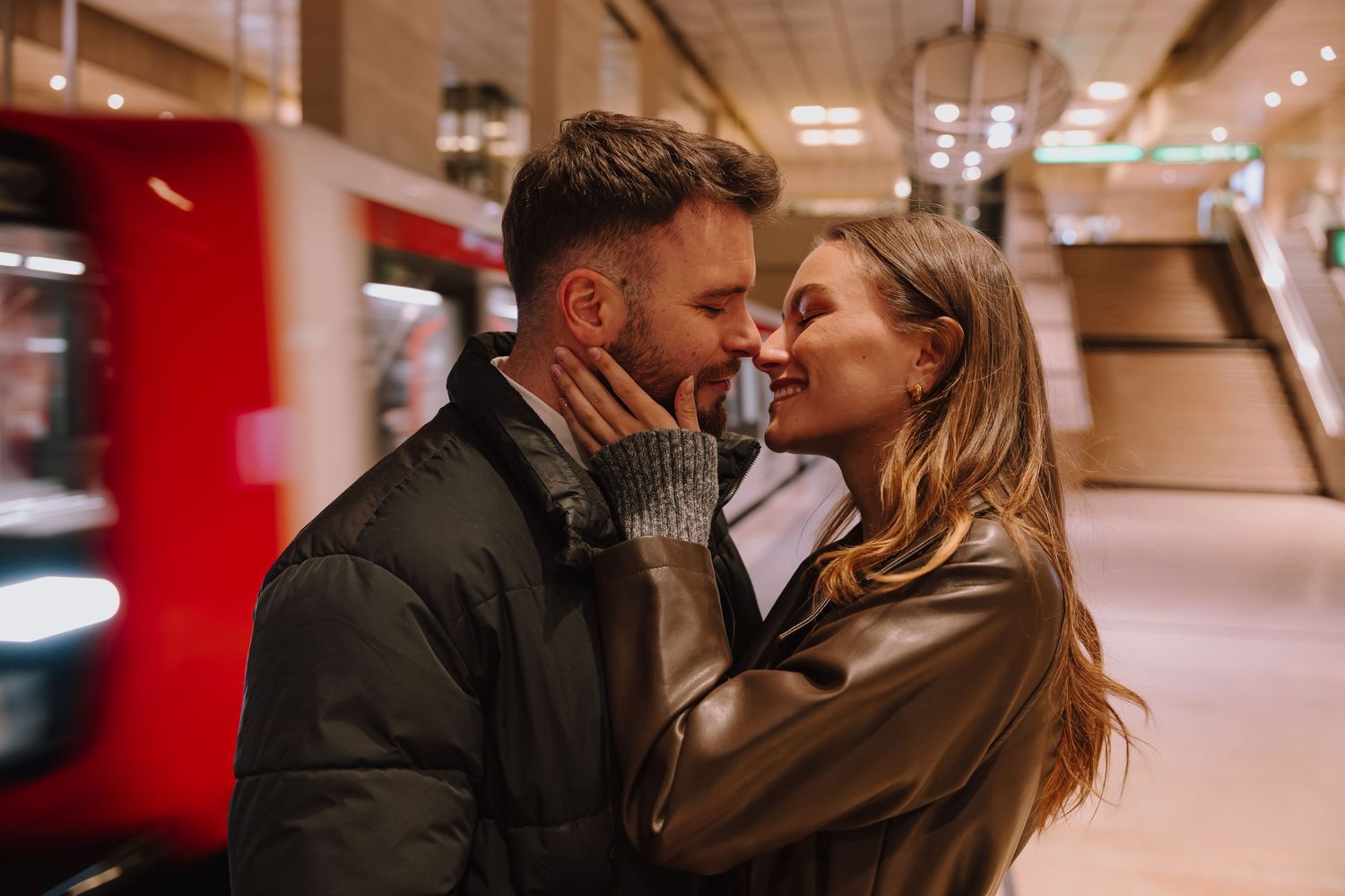 A couple shares a romantic kiss in a warmly lit indoor space near a red wall.